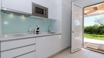 Une cuisine moderne avec des meubles blancs, un four à micro-ondes de la marque Bosch et une porte en verre donnant sur un patio avec vue sur la verdure.