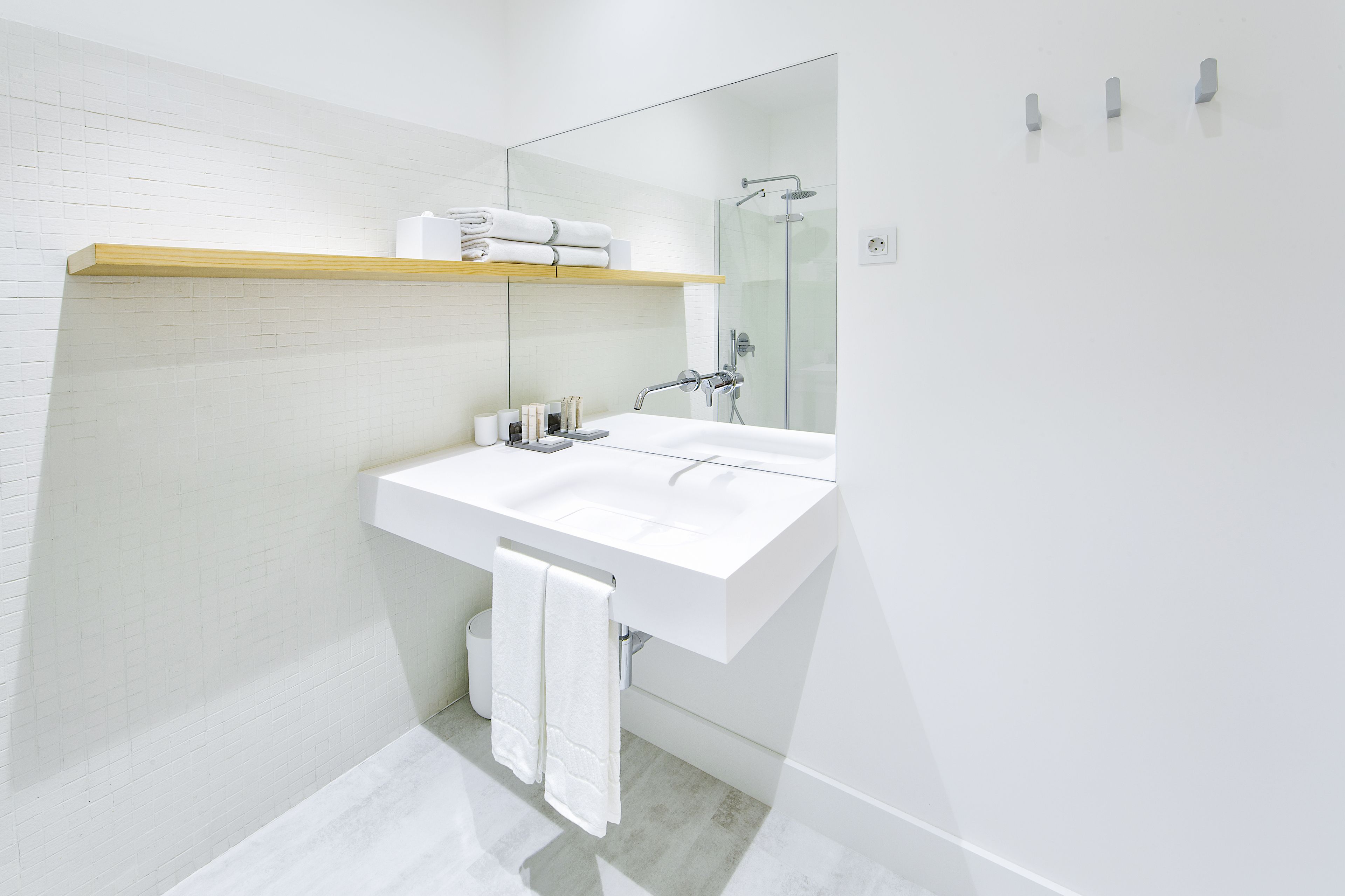 Un baño moderno con un lavabo blanco, una cabina de ducha de vidrio y un estante de madera sobre el lavabo.