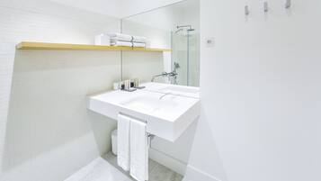 Un baño moderno con un lavabo blanco, una cabina de ducha de vidrio y un estante de madera sobre el lavabo.