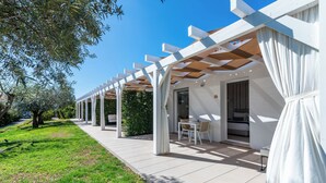 Un espacio de estar al aire libre techado, con columnas blancas, una mesa y sillas.