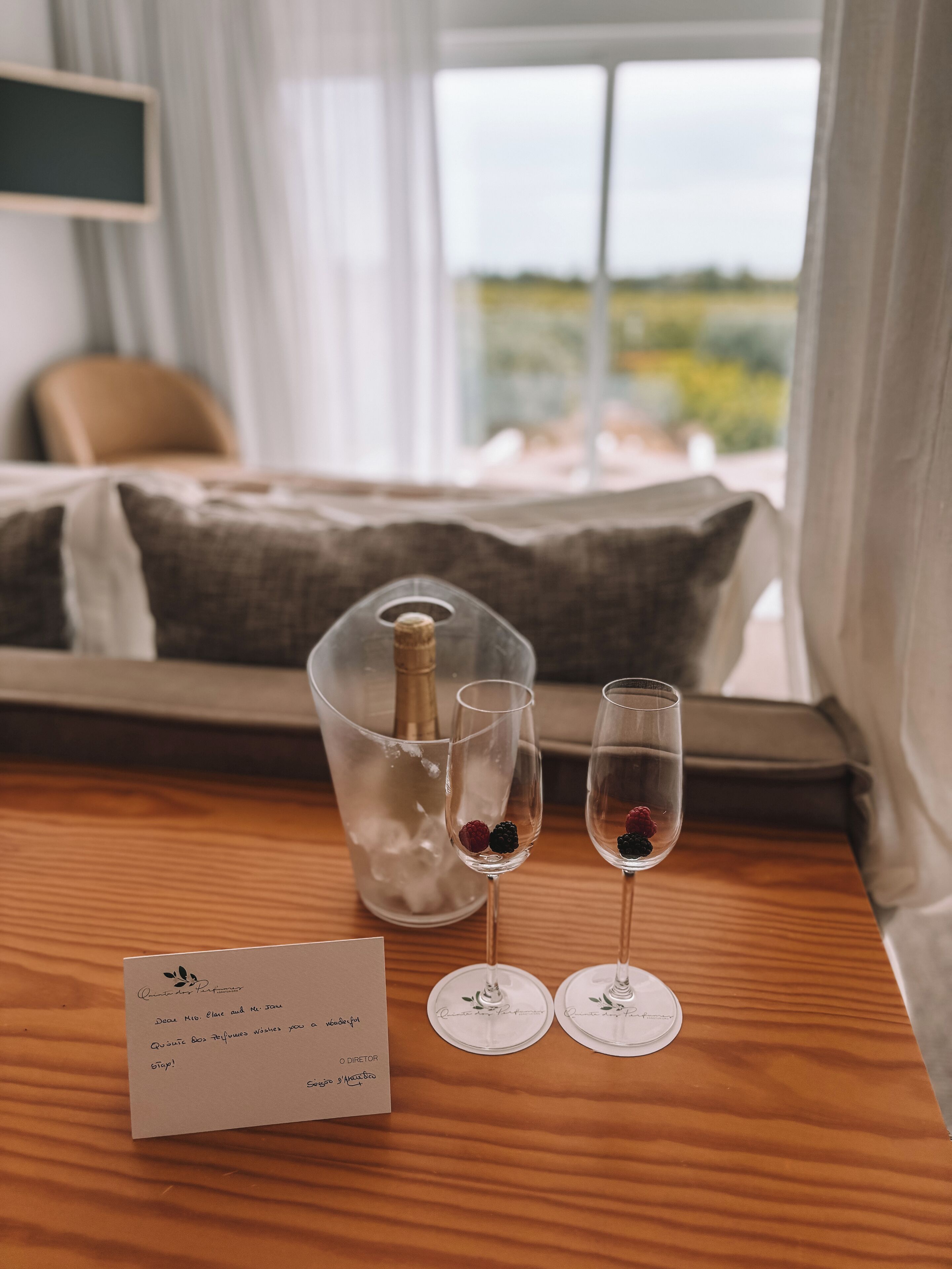 Hotelkamer met een bed, nachtkastje met een champagnefles, twee glazen met bessen en een briefje.