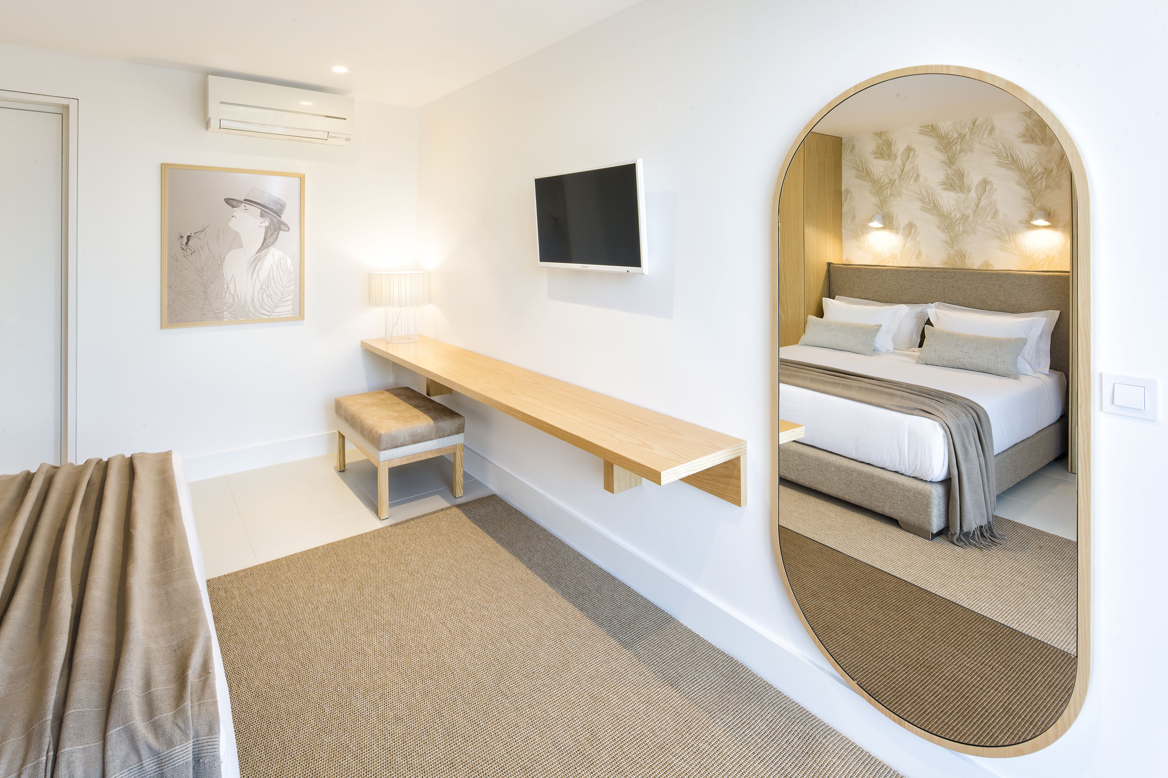 A hotel room with a bed, a desk, a chair, a TV, and a large mirror.