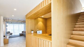 Un interior moderno con un mostrador de recepción de madera, una escalera y un área de descanso con un sofá y una mesa de centro.