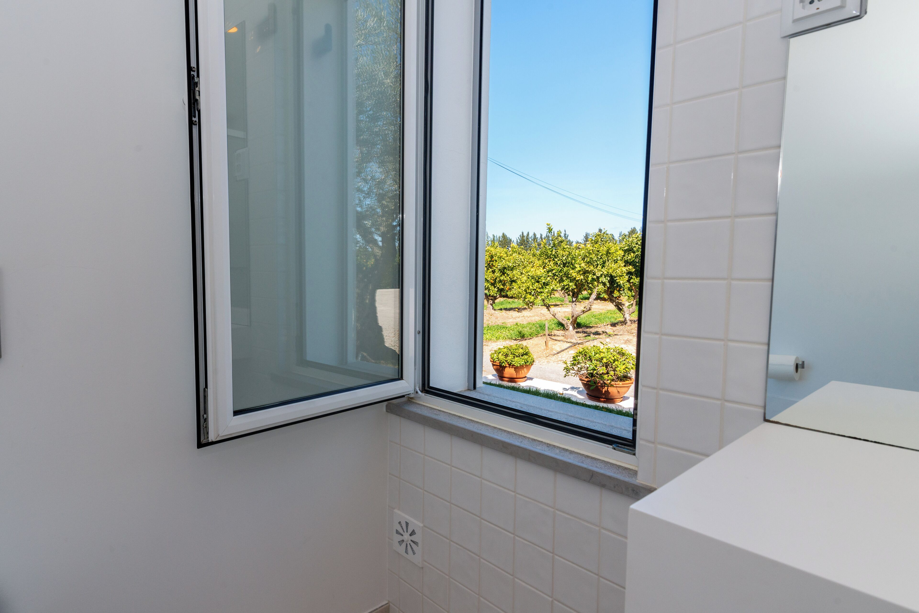 Une salle de bain avec une fenêtre, des carreaux blancs et une vue sur la verdure.