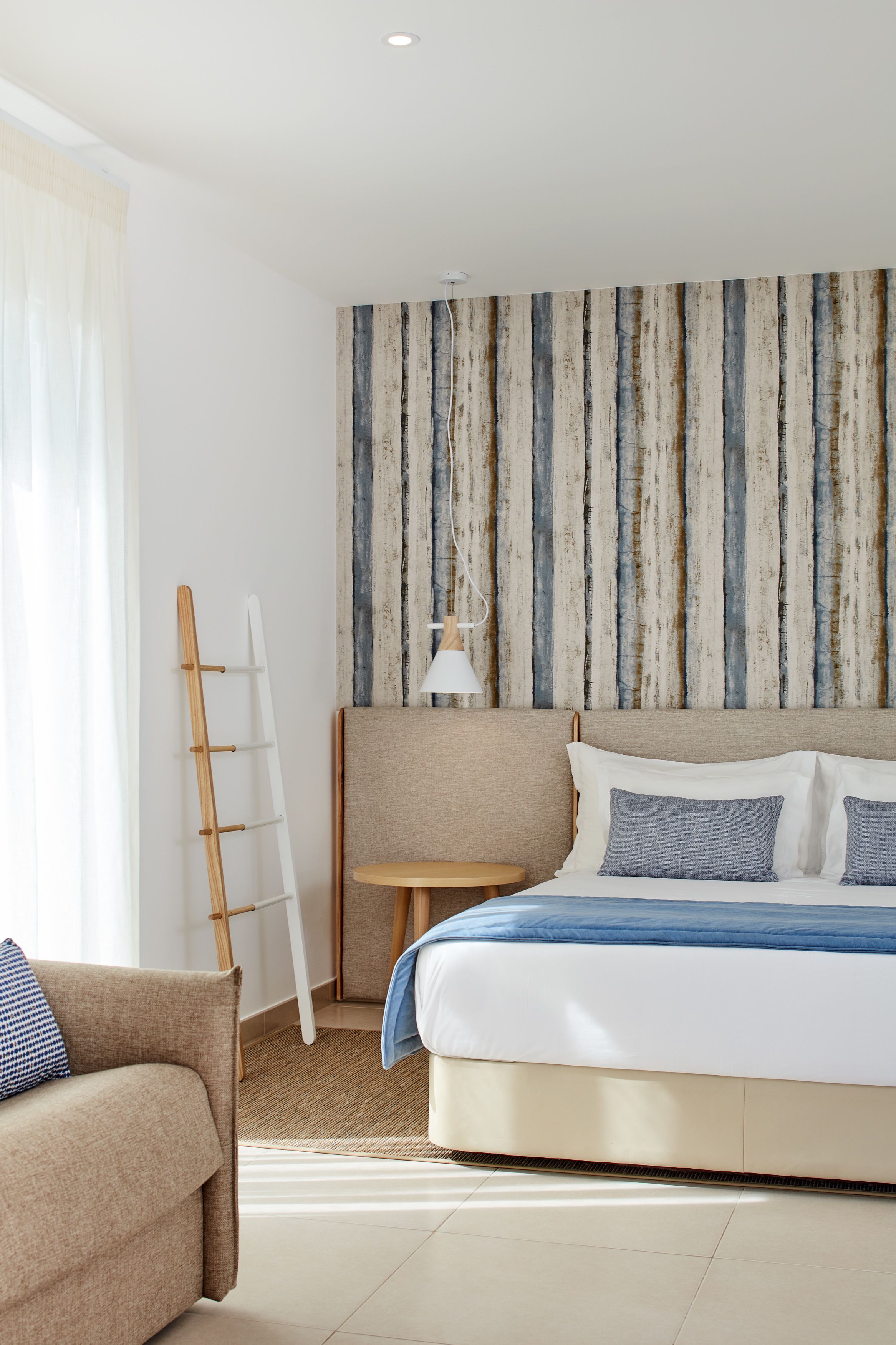 Hotellihuone, jossa on sänky, sohva, lamppu ja raidallinen seinä.