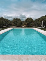 Una piscina al aire libre, sombrillas, sillones reclinables de piscina