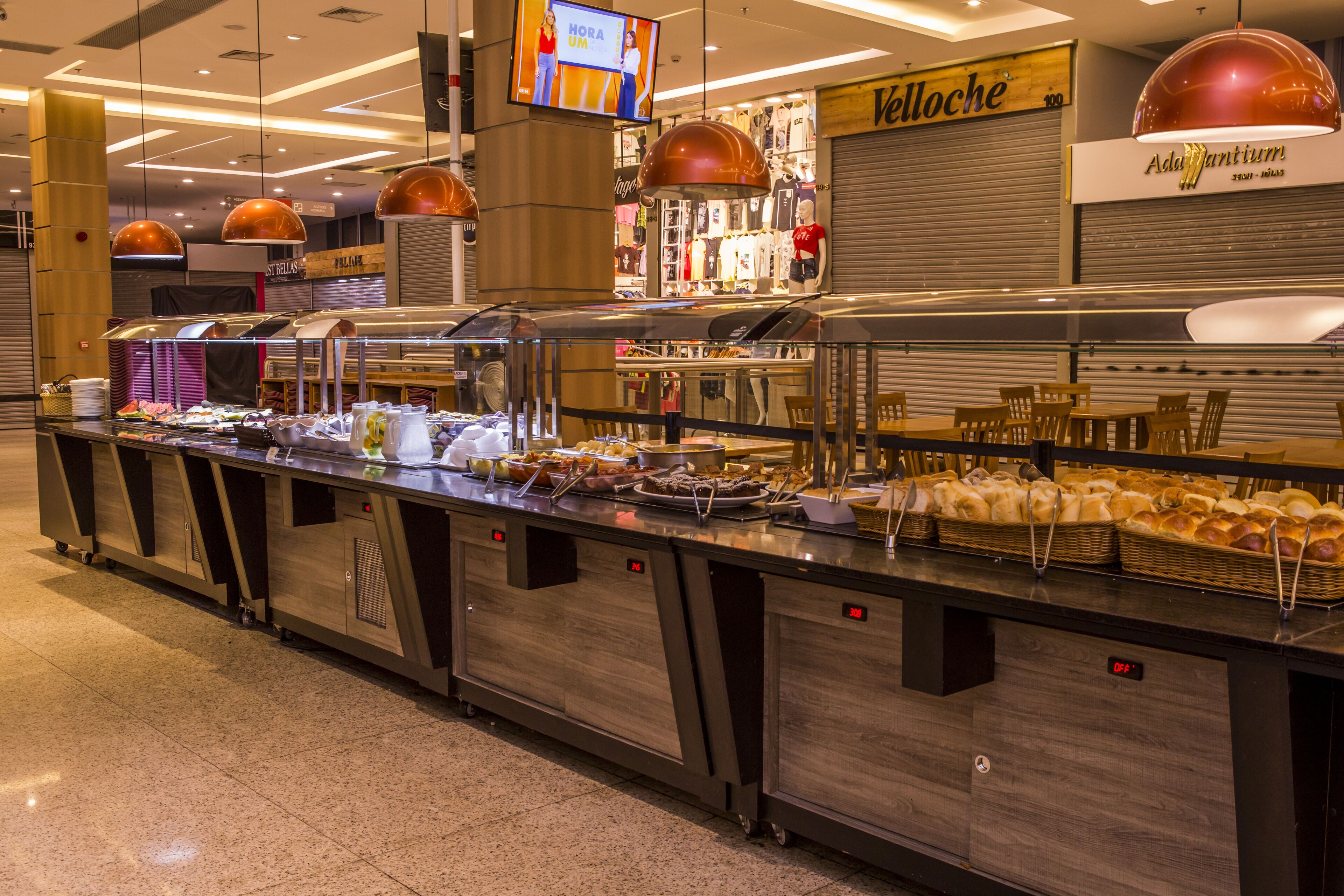 Zona de buffet amb diverses opcions de menjar, una pantalla de televisió i una botiga de roba al fons.