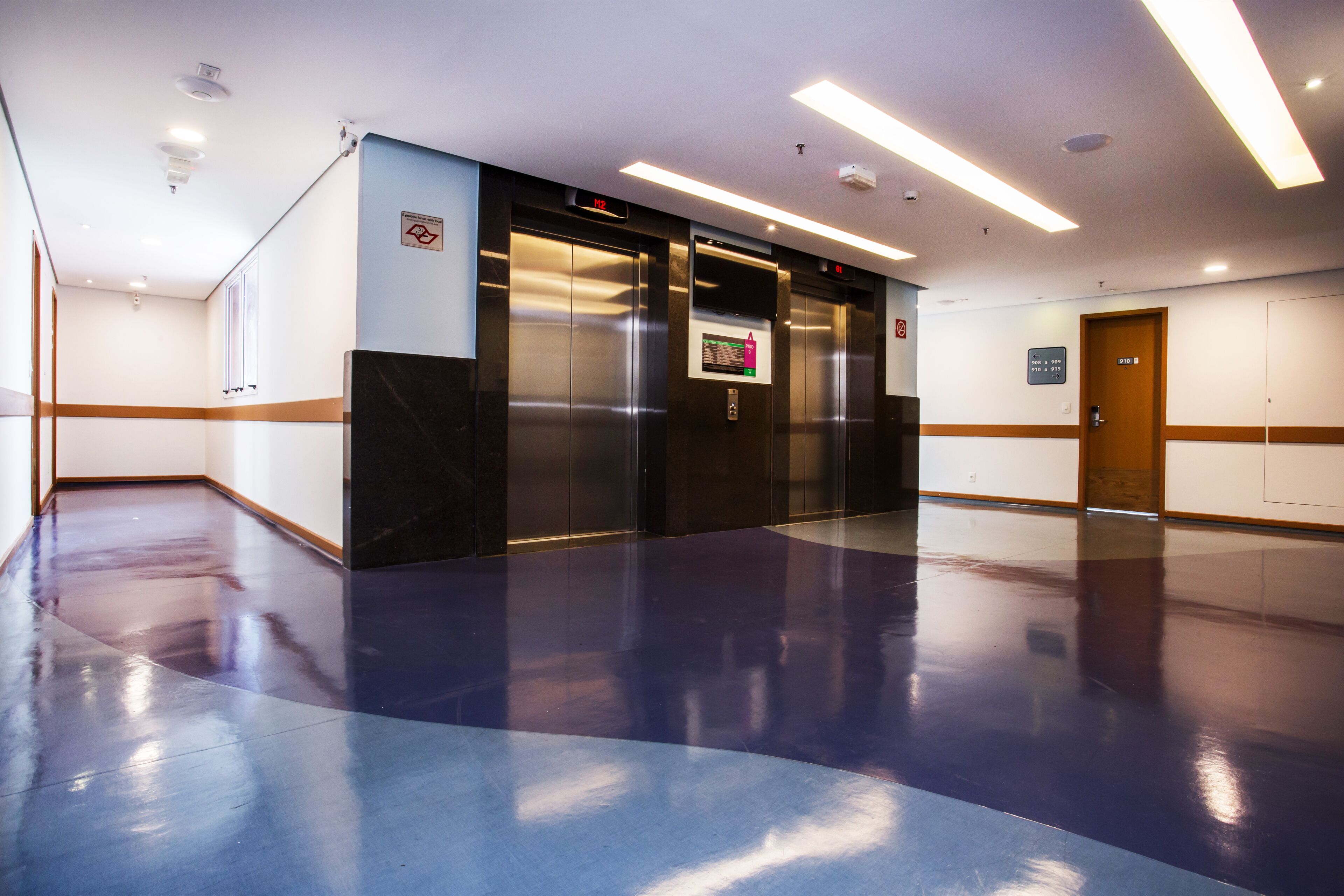 A spacious lobby with a polished floor, two elevators, and a door marked with a sign.