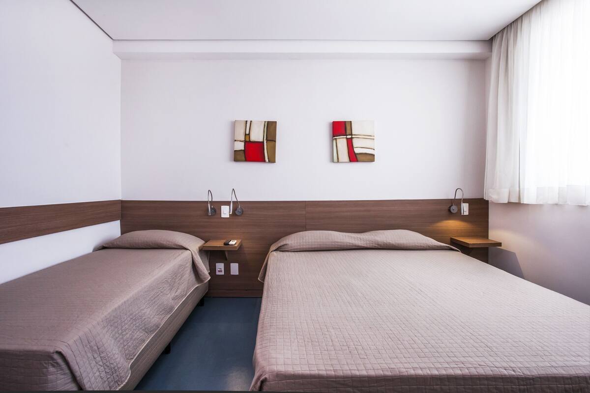 Hotellihuone, jossa on kaksi sänkyä, puinen pääty, yöpöydät ja seinällä abstrakteja taideteoksia.