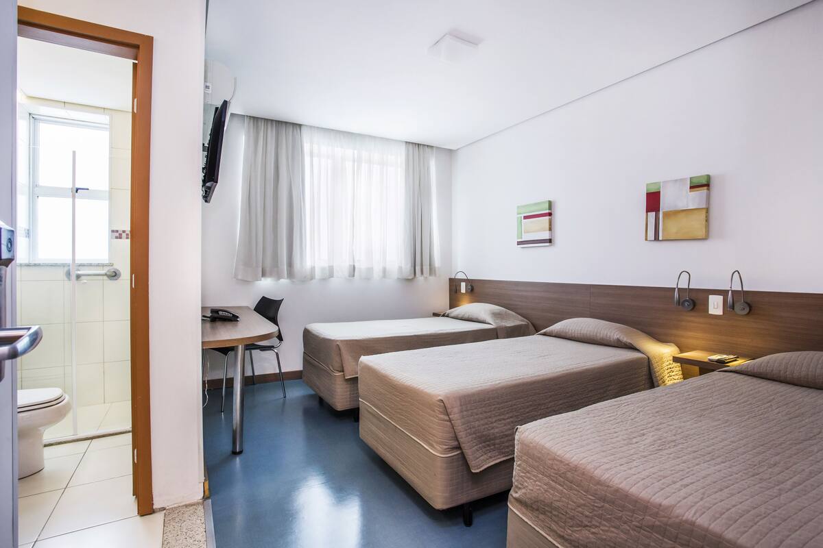 Hotellihuone, jossa on kaksi sänkyä, työpöytä, tuoli, ikkuna verhoilla ja seinälle asennettu televisio.