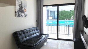 A modern living room with a black leather sofa, a large sliding glass door leading to a pool area, and a framed picture on the wall. - V.O.P. Suite (Koh Samui)