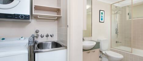 A modern bathroom with a built-in washing machine, a sink, a toilet, and a glass-enclosed shower.