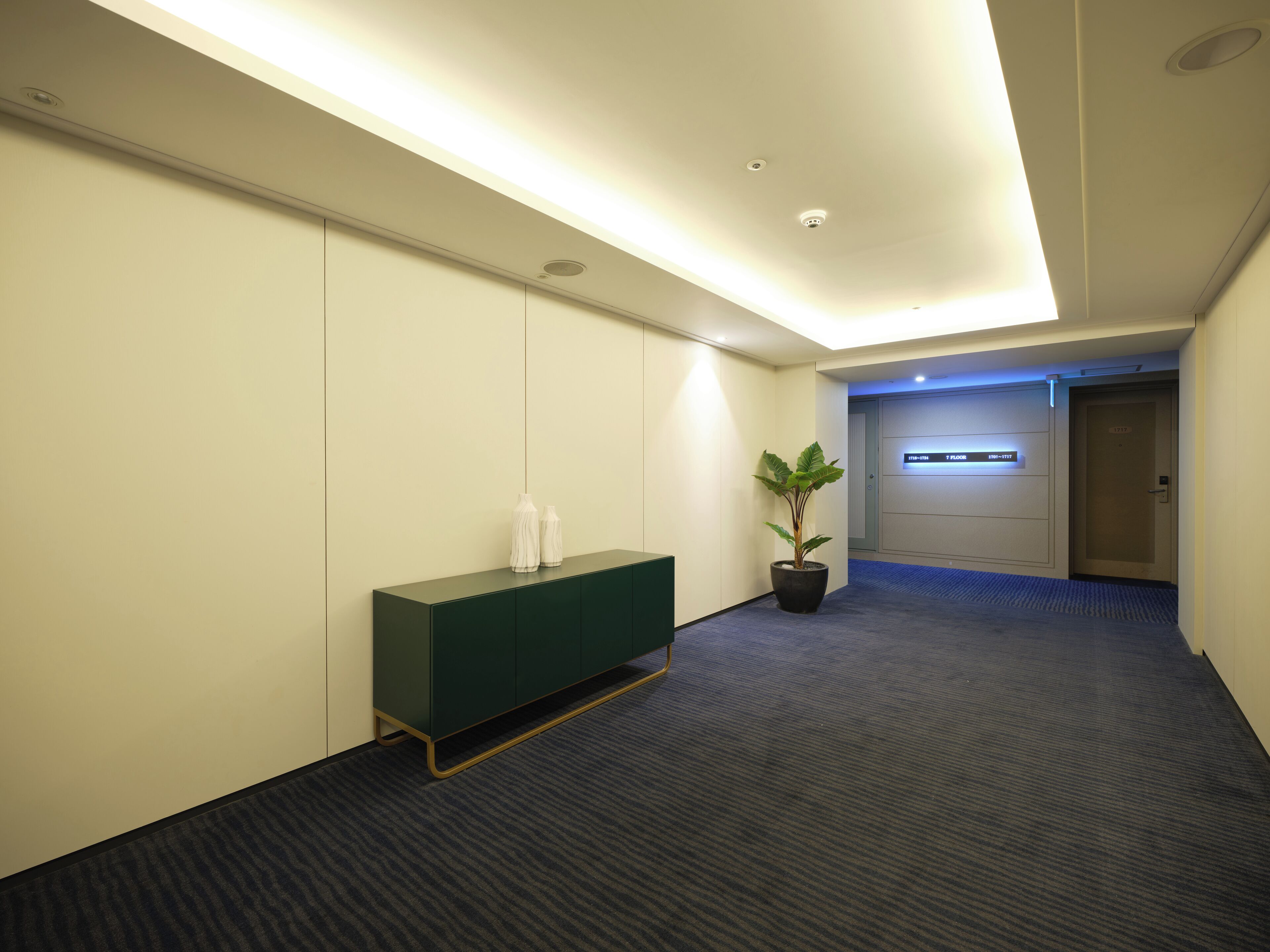 A hotel lobby with a reception desk, a potted plant, and a digital display.