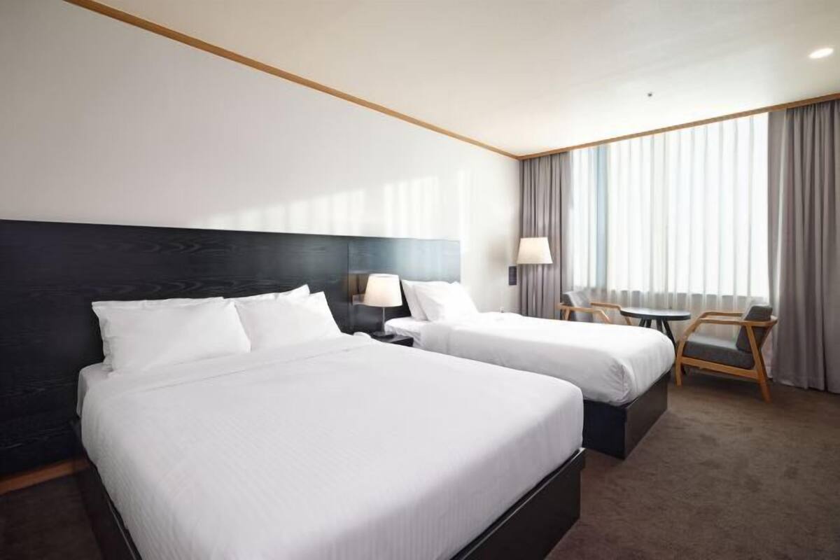 A hotel room with two beds, a desk, a chair, and a large window with curtains.