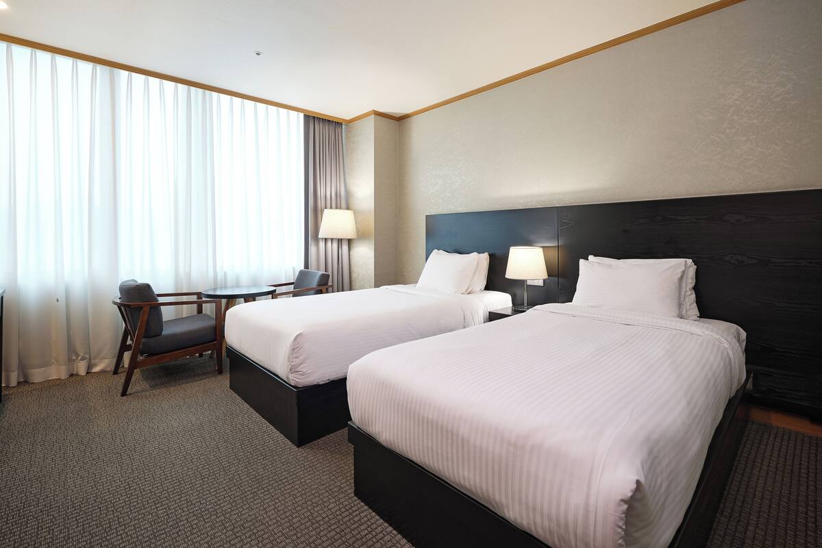 A hotel room with two beds, a desk, a chair, and a window with curtains.