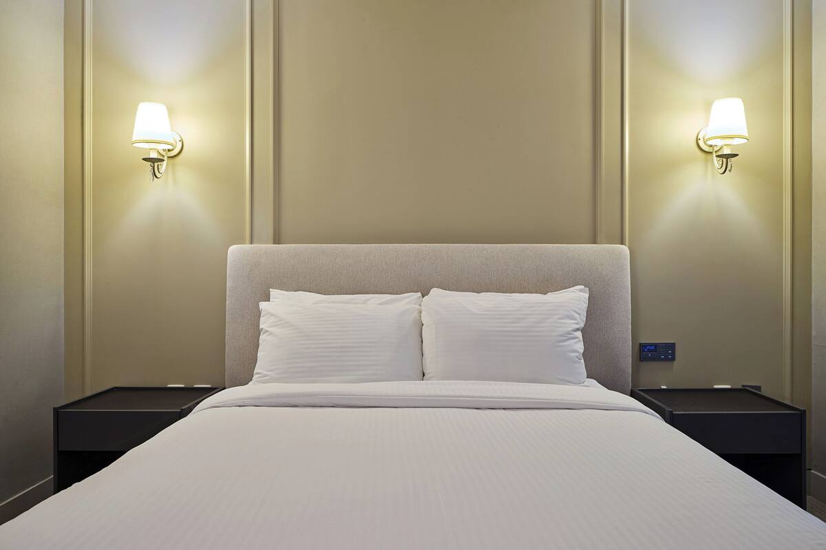 A hotel room with a large bed, two nightstands, and wall-mounted lamps.