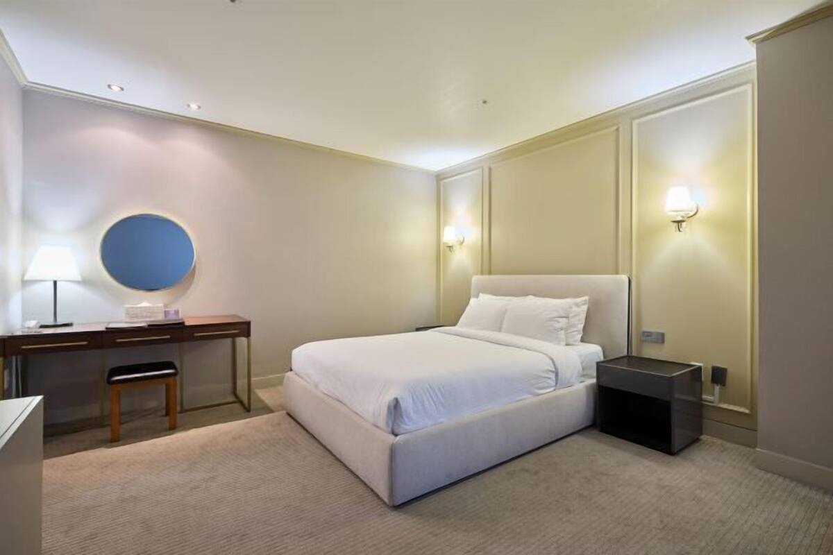 A bedroom with a bed, desk, chair, lamp, and bedside tables.