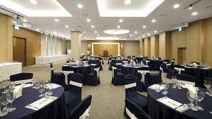 Une salle de conférence avec des tables rondes, des nappes bleu marine et des rubans blancs décorant les chaises.