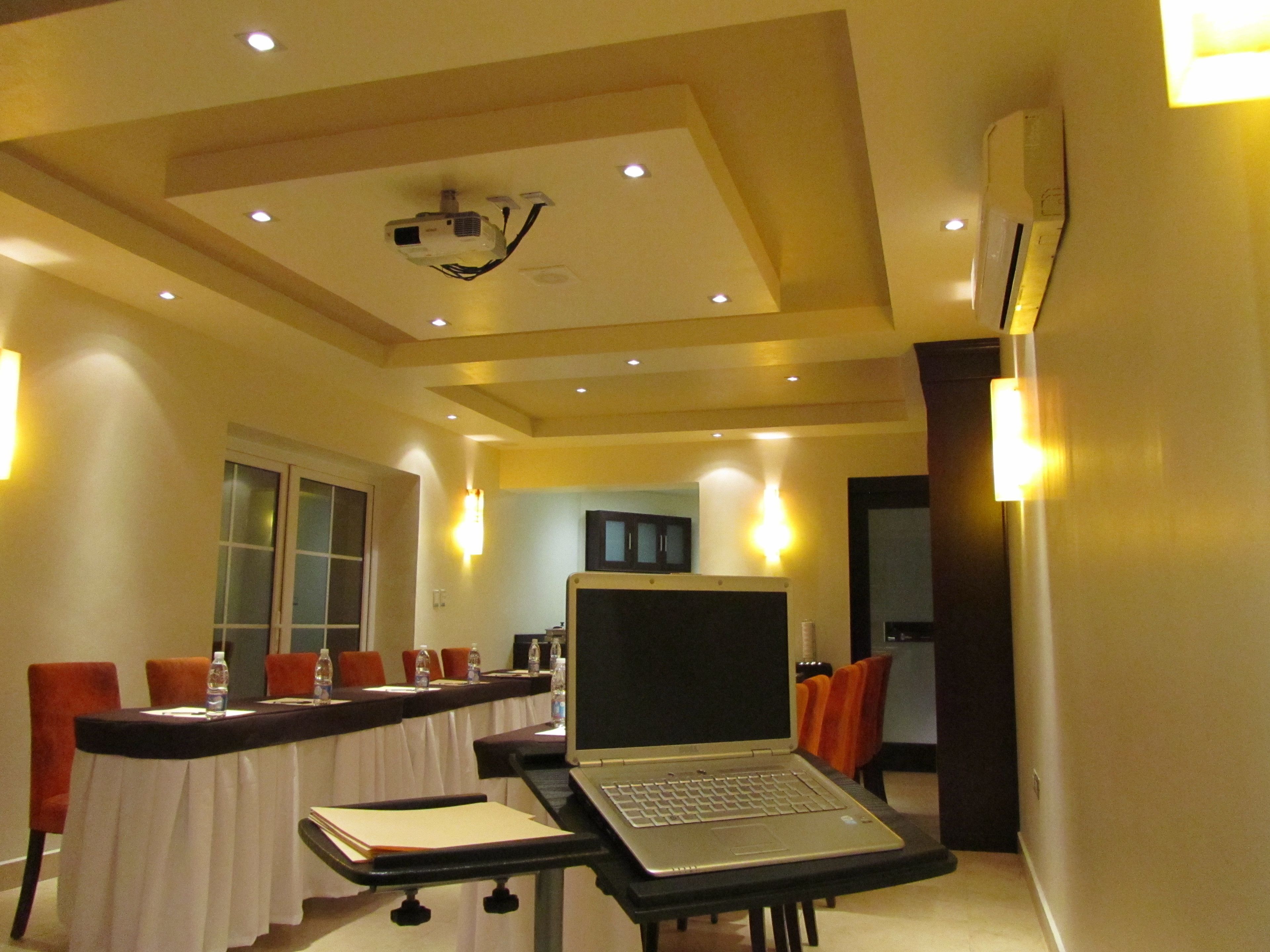 A conference room with a long table, chairs, a laptop on a stand, and a projector on the ceiling.