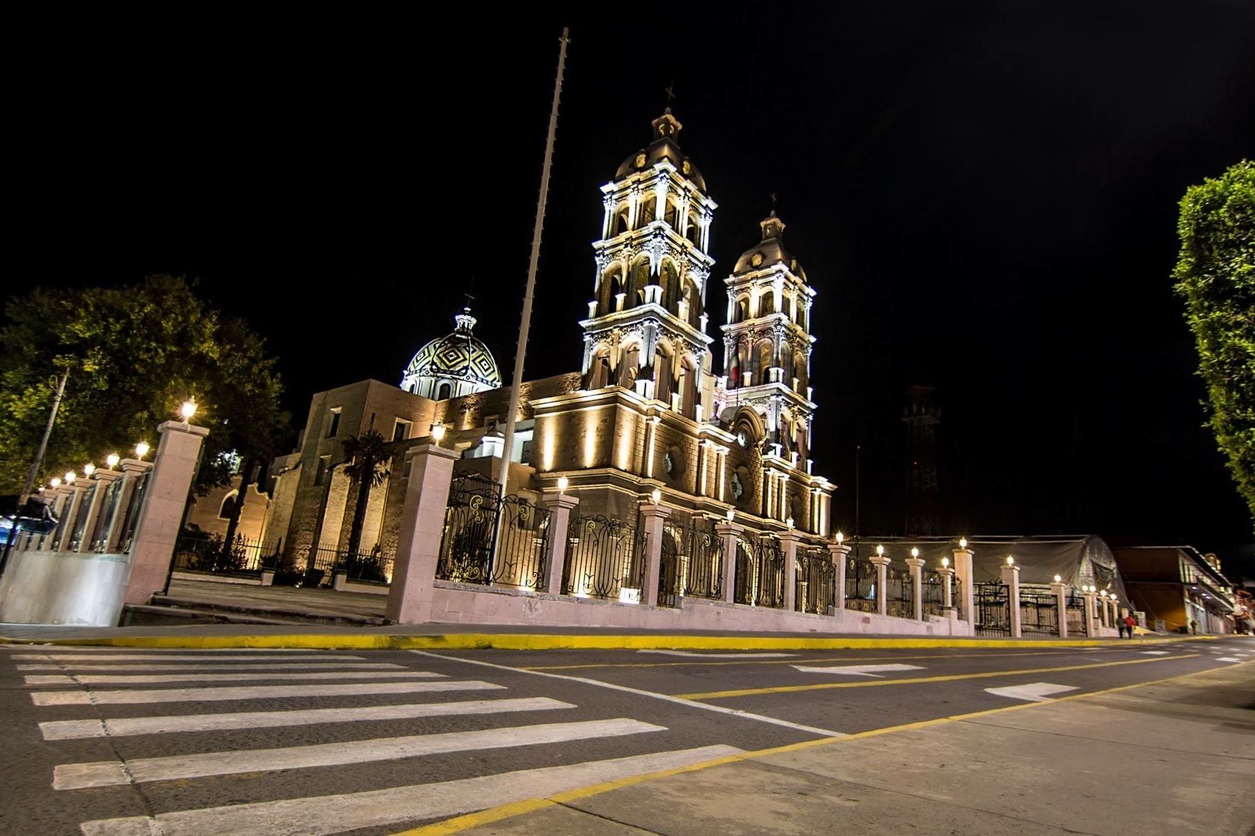 A historic church with two bell towers and a dome, featuring intricate architectural details and illuminated at night.