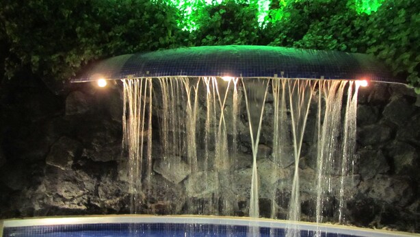 A waterfall feature with water cascading over a tiled structure into a pool. - Hotel Colonial (Teziutlan)