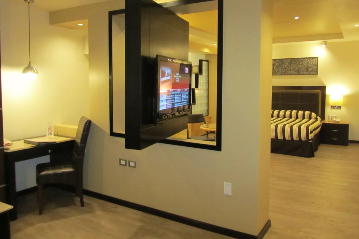 A hotel room with a desk, chair, television, bed, and a mirror.