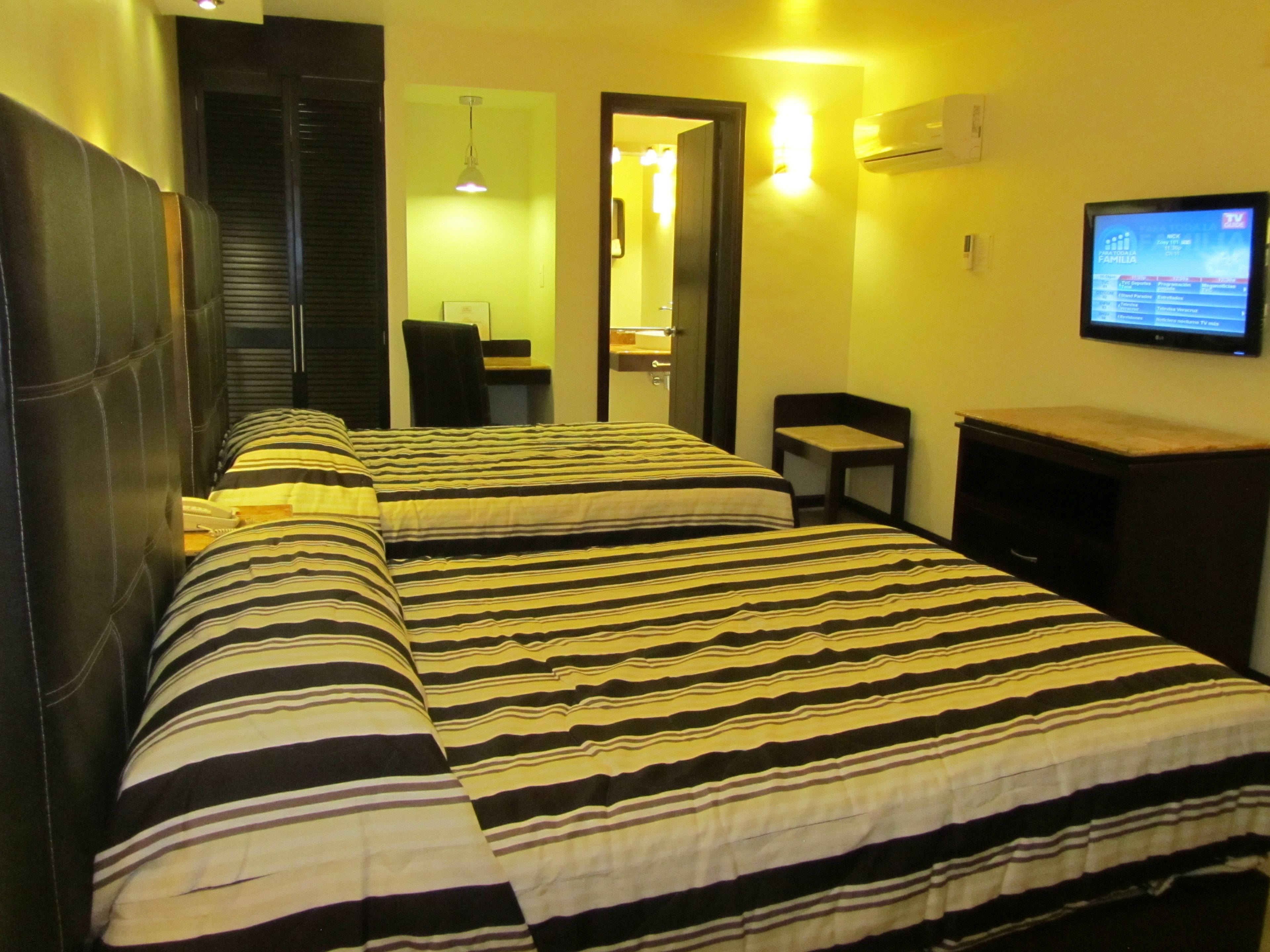 A hotel room with two beds, a desk, a chair, a TV, and a mirror.