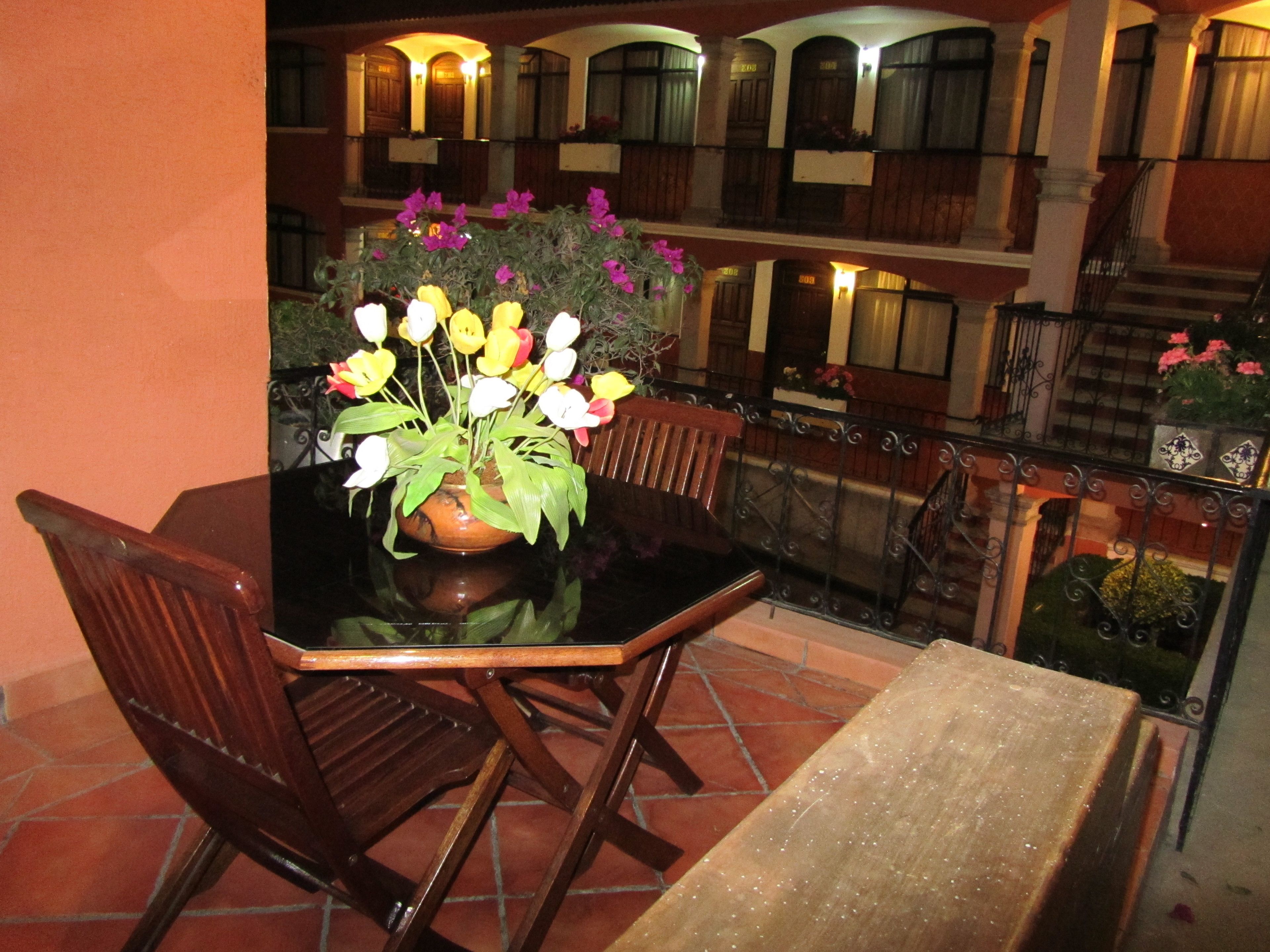 Un comedor con una mesa y sillas, una planta en maceta con flores, y vistas a un edificio con balcones y ventanas.