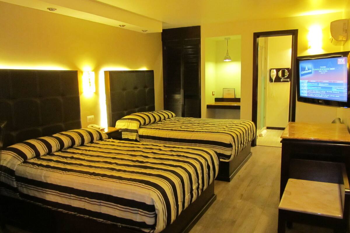 A hotel room with two beds, a desk, a television, and a mirror.