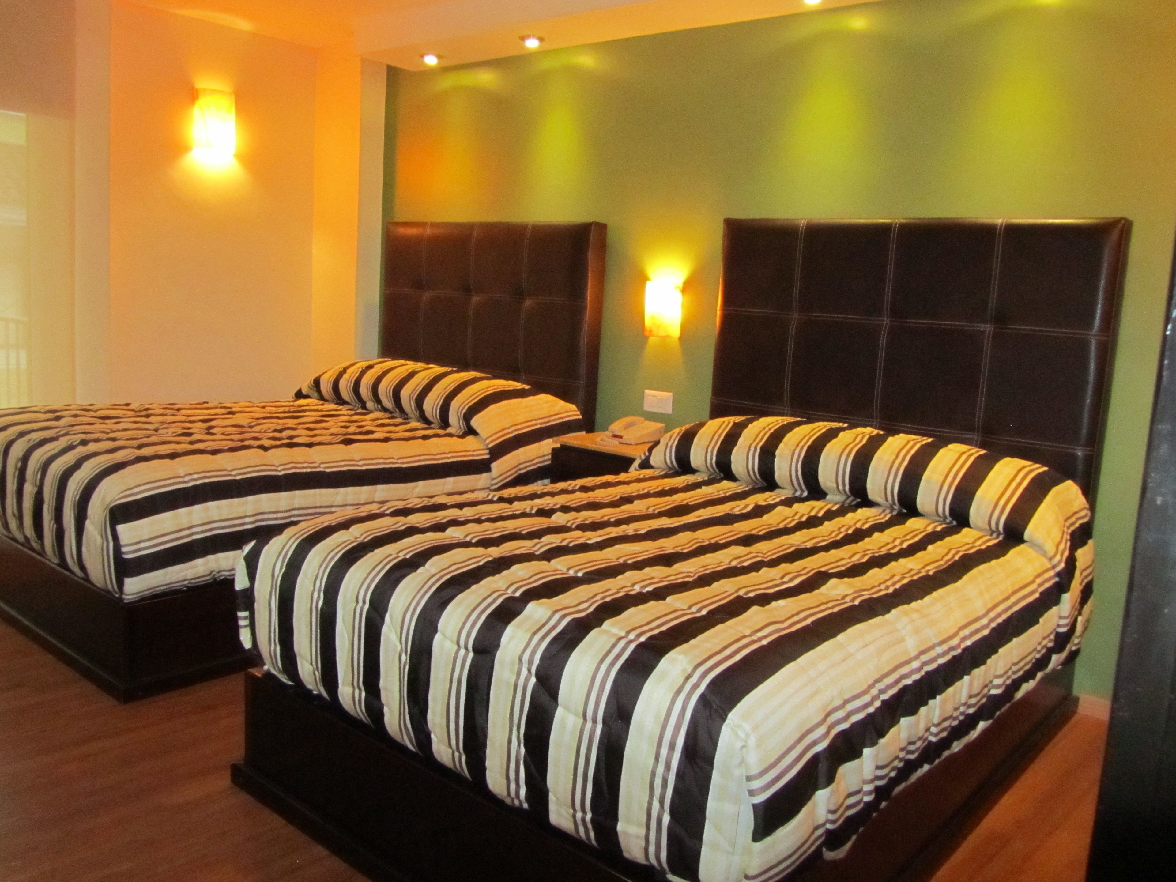 Ein Hotelzimmer mit zwei Betten, jeweils mit gestreifter Bettwäsche, einem dunklen Kopfteil und einer an der Wand befestigten Lampe.