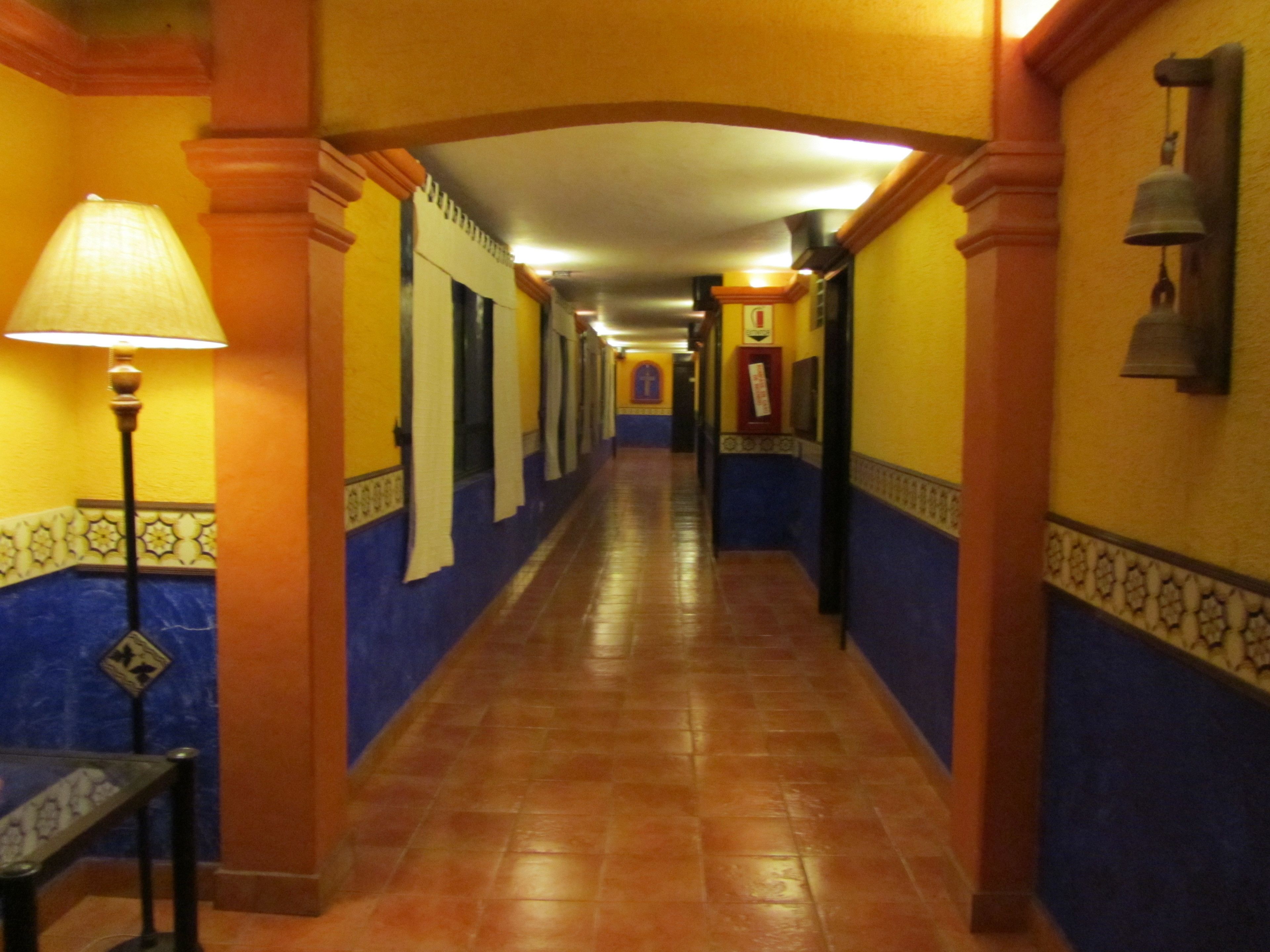 Un pasillo con suelo y paredes de baldosas, que presenta una lámpara y un timbre en la pared.
