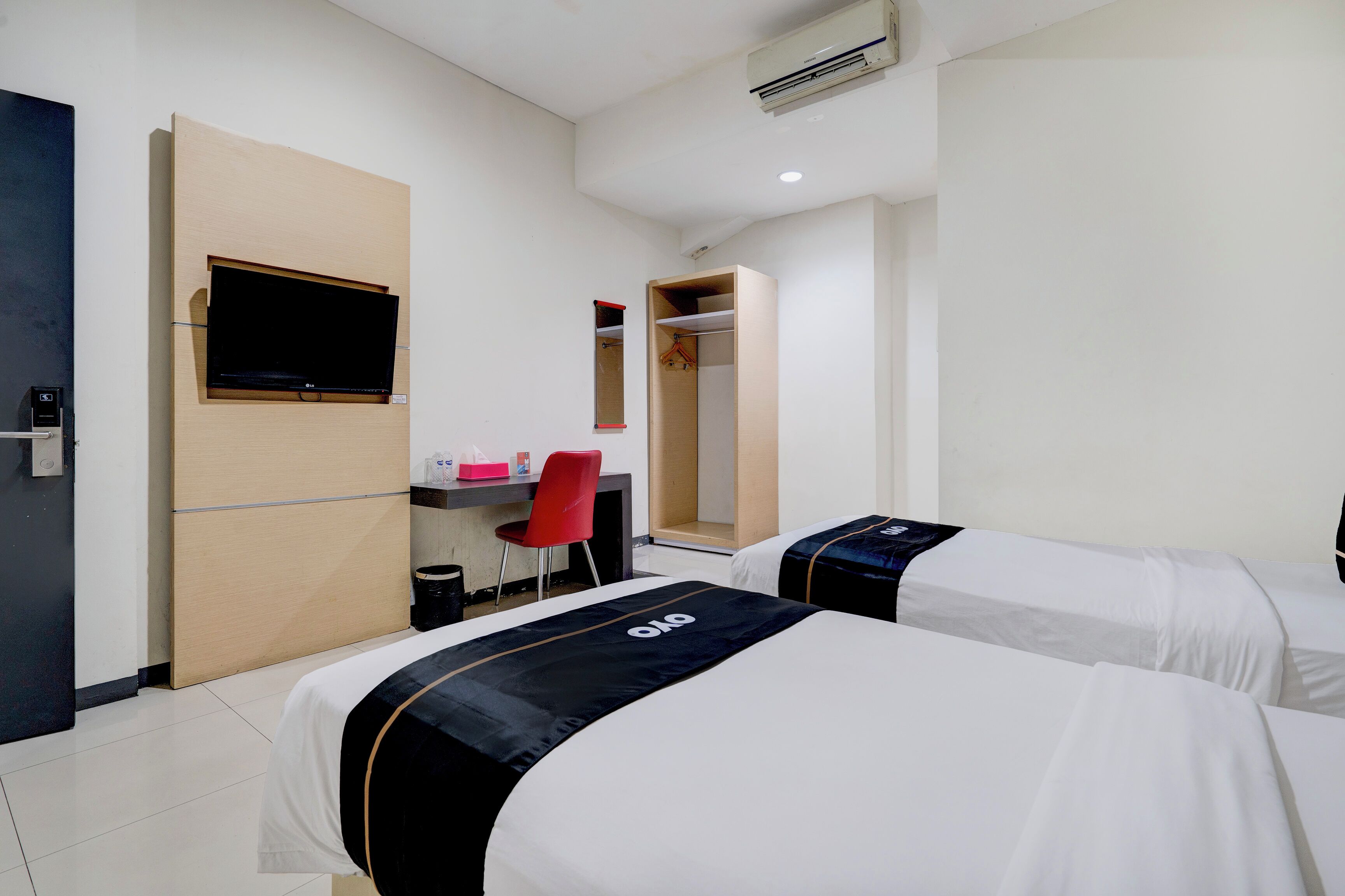 A hotel room with two beds, a desk with a chair, a TV mounted on the wall, and a wardrobe.