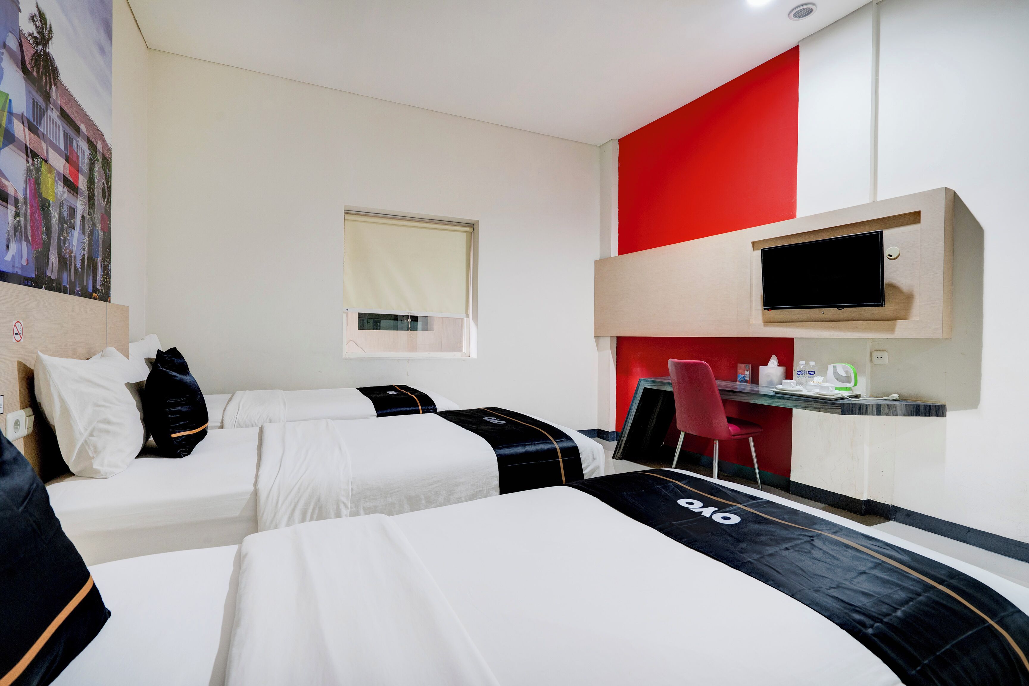 A hotel room with two beds, a desk with a computer, a chair, and a TV mounted on the wall.
