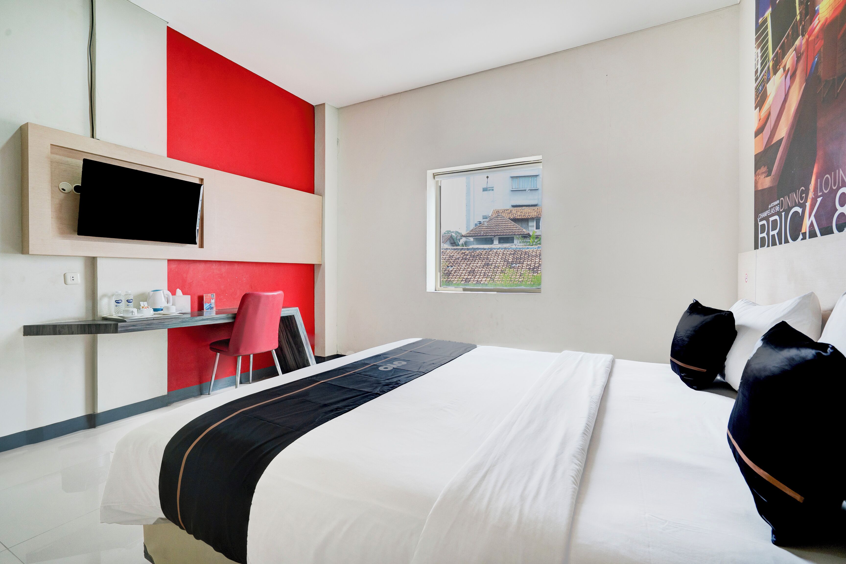 A hotel room with a bed, a desk with a chair, a TV, and a window with a view of buildings.