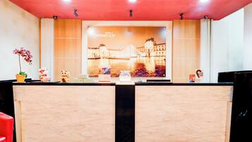 A hotel reception desk with a large poster of the Louvre Pyramid, a potted plant, and a small statue.