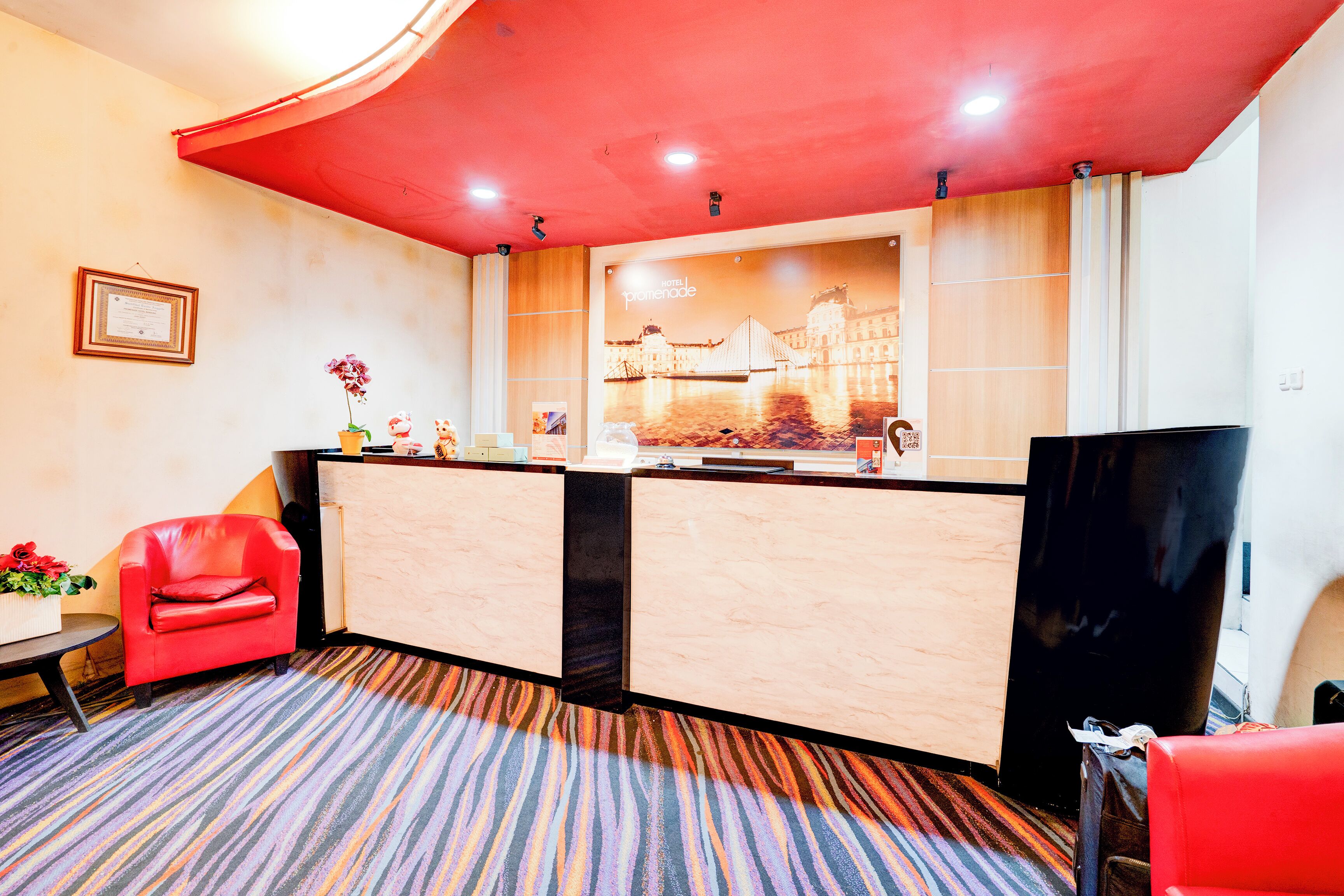 A reception area with a red chair, a reception desk, and a large poster of a building.
