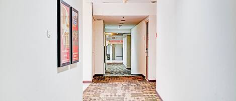 A hotel hallway with framed pictures on the walls, carpeted flooring, and a visible exit sign.