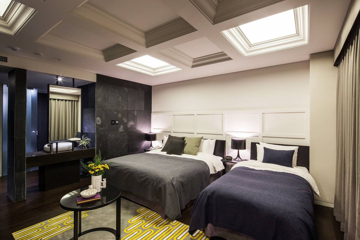 A modern hotel room with a large bed, a smaller bed, a desk, and a mirror.