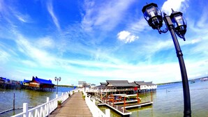 A wooden pier extending into a body of water with a white railing, a row of potted plants, and a row of buildings with blue roofs in the background. - Scuba Tiger Semporna Holiday Resort (Semporna)