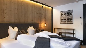 Una cama bien hecha con ropa de cama blanca y gris oscuro, un cabecero de madera y una lámpara fijada a la pared.