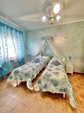 Un dormitorio con dos camas individuales, una cama con dosel, una mesita de noche y una lámpara de techo.