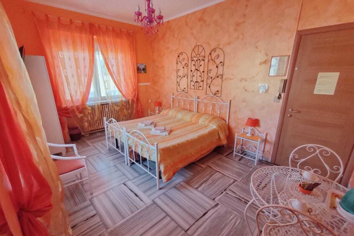 A bedroom with a bed, a nightstand, a chair, a chandelier, and a door.