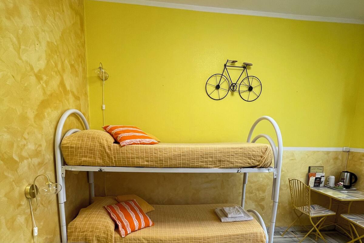A bunk bed room with a yellow wall, a bicycle decoration, a small table, and a patterned floor.