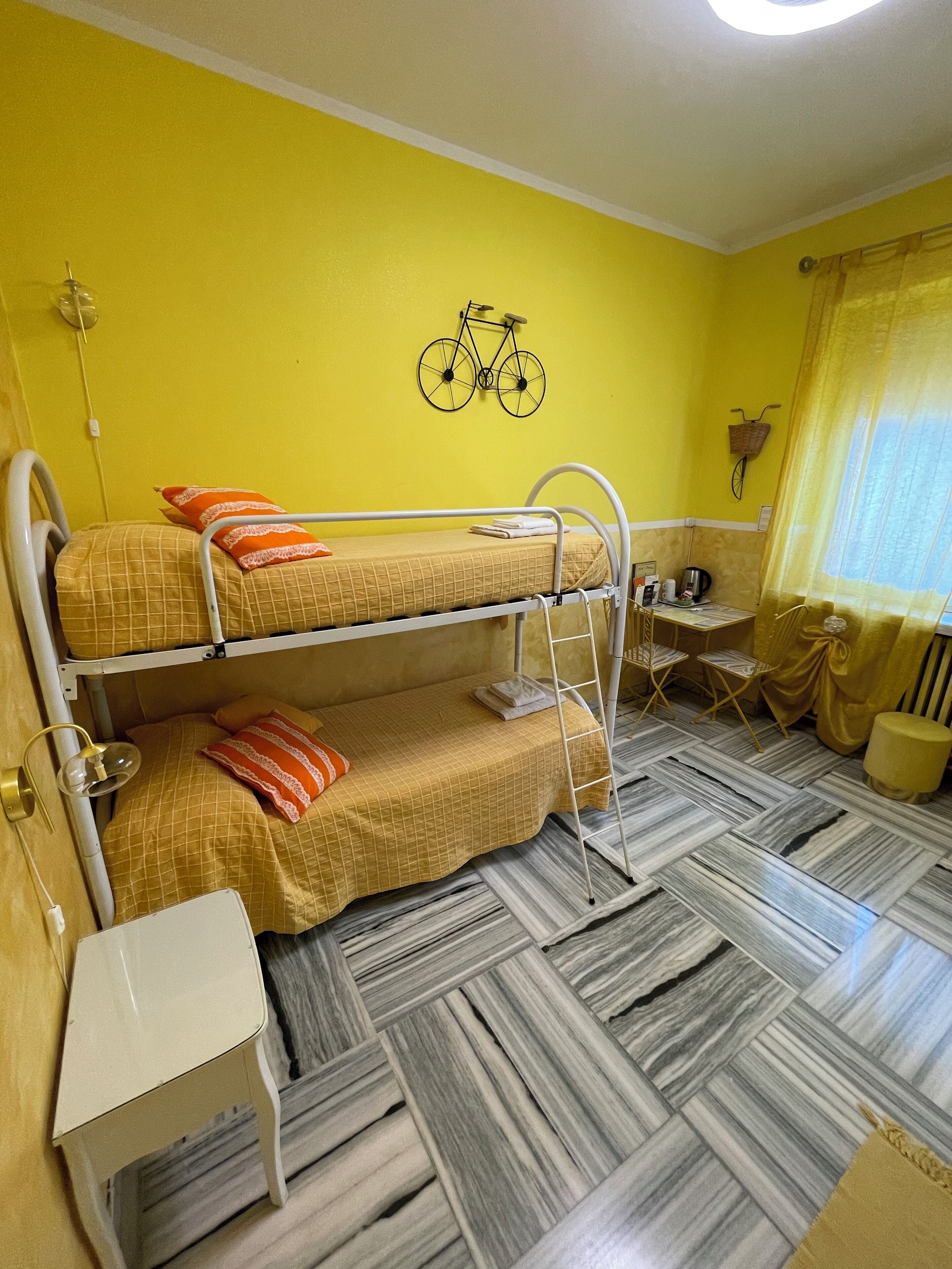 A bunk bed room with a bicycle wall decoration, a small desk, and a window with curtains.