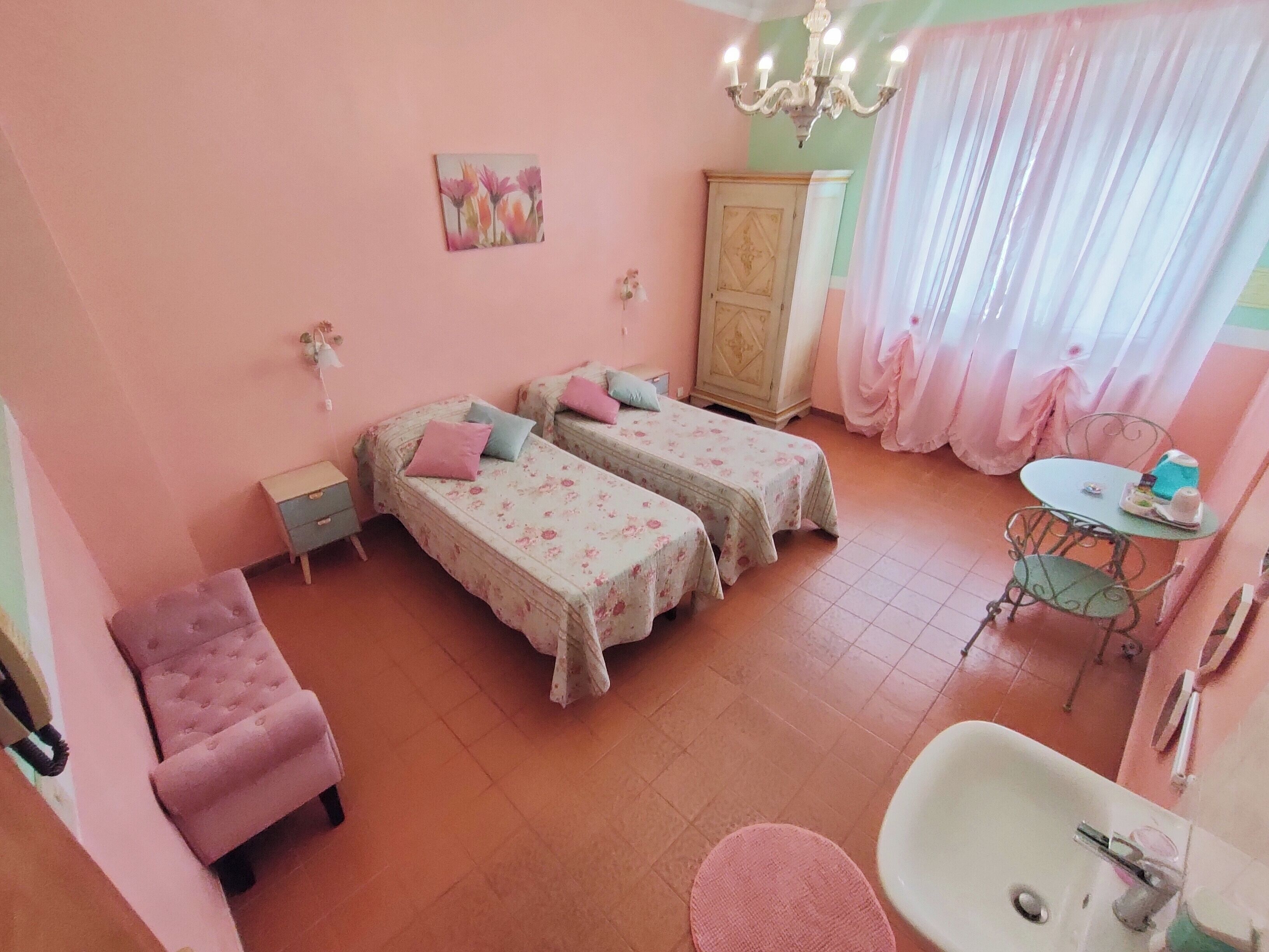 Een roze kamer met twee bedden, een kaptafel met wastafel, een stoel en een kroonluchter.