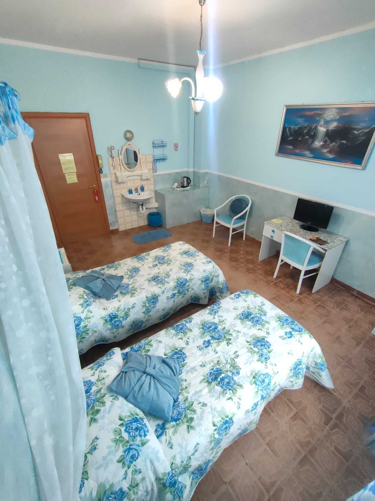 A bedroom with two beds, a desk, a chair, a television, and a bathroom.