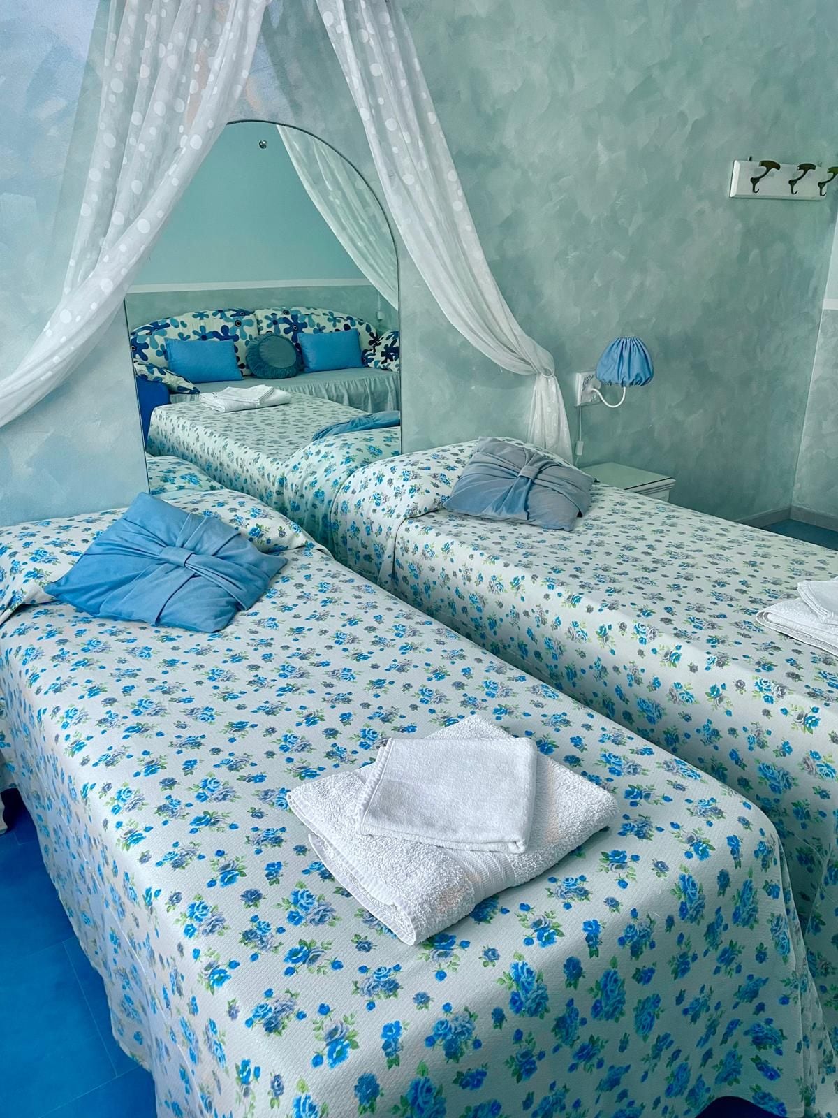 A bedroom with two beds, each with a floral bedspread, a nightstand with a lamp, and a mirror on the wall.