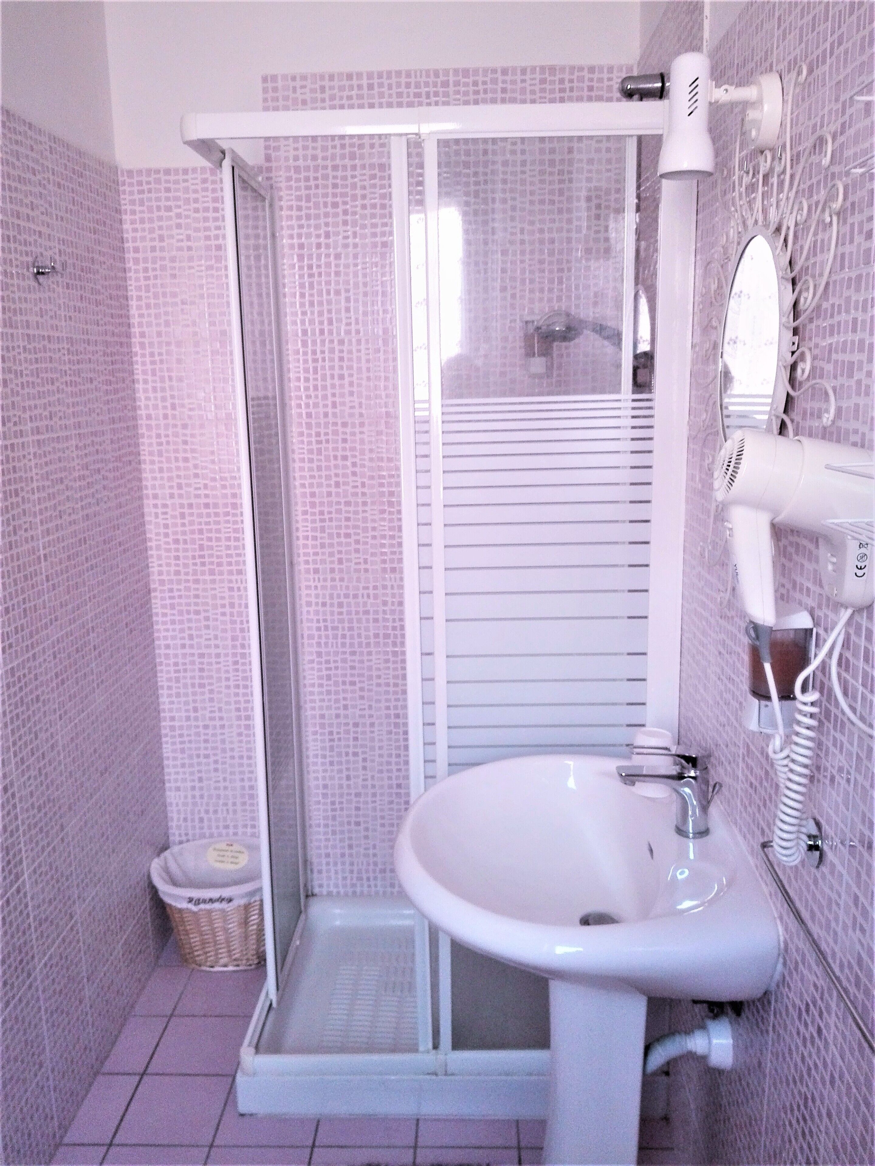 A bathroom with a white sink, a glass shower enclosure, and a hairdryer mounted on the wall.