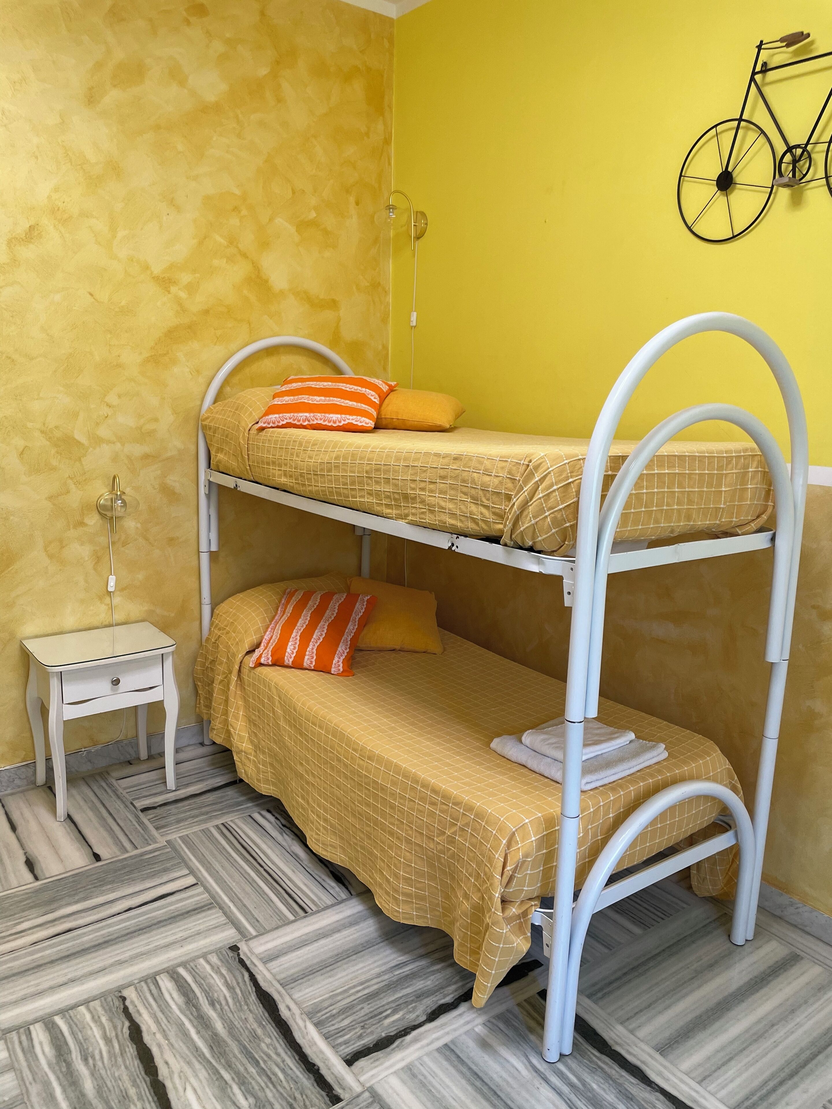 Una cama litera de dos plazas, una mesita de noche pequeña y una bicicleta fijada a la pared.