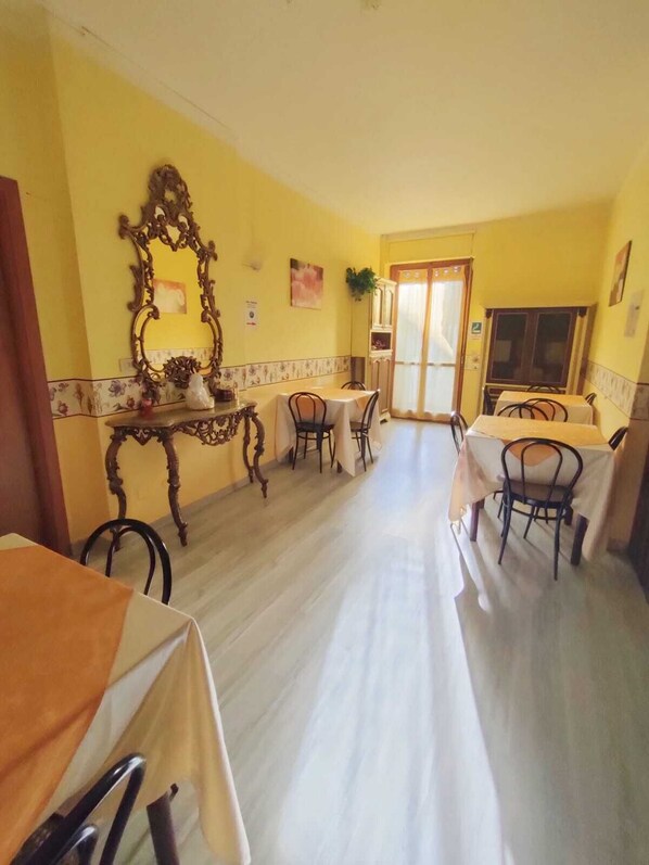 Un comedor con paredes amarillas, un espejo grande y decorativo, y un armario de madera. Hay dos mesas con sillas, y una puerta que da a otra habitación.